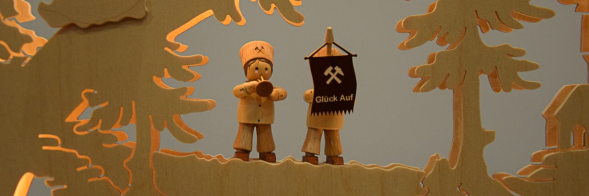 Schwibbogen Bergmann – Nahaufnahme von zwei Bergmännern, einer mit Trompete und einer mit  „Glück Auf“-Fahne