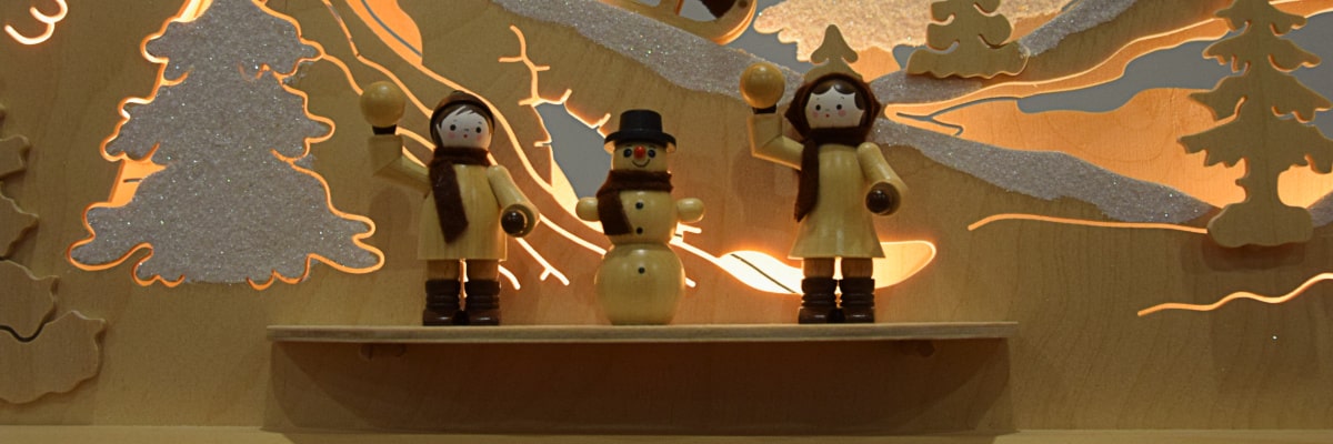 Schwibbogen Winterlandschaft – Nahaufnahme von drei Figuren, zwei werfen Schneebälle Richtung Betrachter